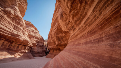 A sun-drenched path winds through a breathtaking desert canyon, flanked by ancient sandstone formations, leading towards a vast, expansive panorama