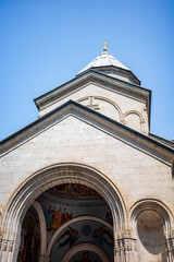 Elegant Orthodox church architecture featuring a stone dome crowned with a golden cross, intricate arched details, and religious frescoes beneath the entrance. A faith, history and unique design