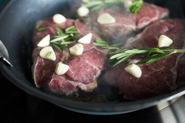 Beef steaks with garlic and rosemary in a frying pan.