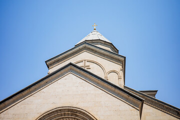 Elegant close-up of a historic church dome featuring a golden cross, soft beige stone architecture, and intricate details, beautifully set against a clear blue sky. Perfect for themes of faith, spirit