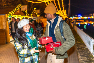 Young multiethnic couple exchanging christmas gifts at christmas market