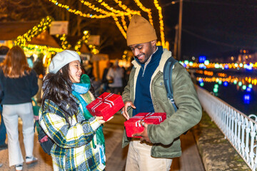 Happy multiethnic couple exchanging christmas gifts at christmas market