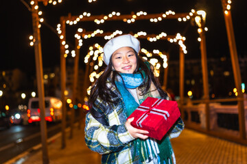 Young woman holding christmas gift under city lights decoration