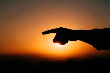 オレンジの夕日を指す影の手のシルエット