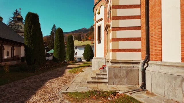 Exterior of the Sinaia Orthodox Monastery, Sinaia, Transylvania, Romania, presenting stone and brick volumes, arched porticos within tranquil monastic grounds and landscaped paths