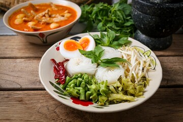 Kanomjeen namya krati ,Rice vermicelli with minced fishes ,Chicken feet,meatballs and coconut milk in red curry on ceramic plate side dish with vegetables and boiled egg