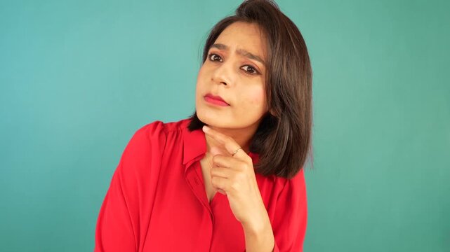 Closeup of confused young Indian woman girl looking at camera pointing finger signalling you with unsure thoughtful face expression, isolated over blue background.