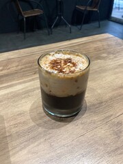 Glass of Cappuccino Coffee with Foam on Wooden Table in Modern Cafe Interior