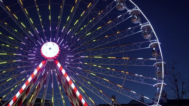 Ferris wheel rotating at night features vibrant purple and yellow lights in bayonne, france, creating a festive atmosphere