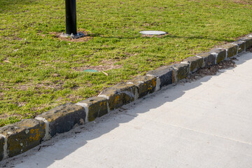 Stone curb edging between a concrete footpath and grassy park. Concept of urban infrastructure, landscape design, and public space maintenance.