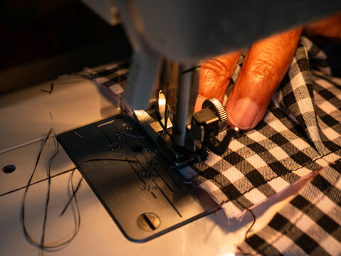 Elderly Woman’s Hands Sewing Fabric with Electric Sewing Machine. Senior Labor and Handicraft Work.