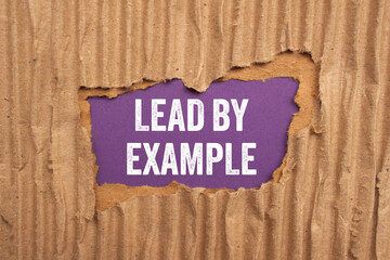 Lead by example message written on ripped torn cardboard paper on purple background. Conceptual...