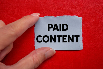 Paid content message written on ripped torn grey paper piece on red background. Conceptual paid...