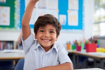 Excited young indian schoolboy raising hand in colorful classroom. Smiling elementary male student answering question during lesson at school desk