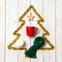 Festive arrangement of a red mug, green scarf, white candle, and golden tinsel shaped like a Christmas tree