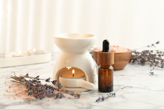 Aroma lamp with burning candle, essential oil, sea salt and lavender flowers on white marble table, closeup