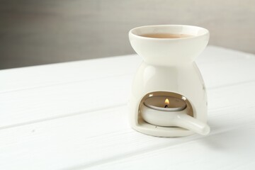 Aroma lamp with burning candle on white wooden table against grey background, closeup. Space for text