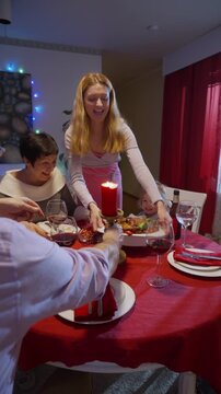 Family Christmas dinner at home. Woman serving roast turkey with vegetables on festive holiday table with candles, wine glasses, and happy relatives. Warm cozy atmosphere of winter celebration