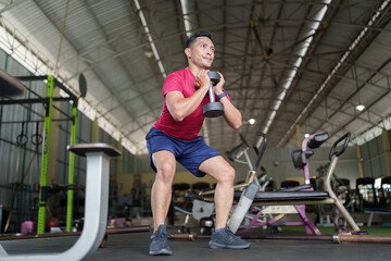 Strength Training. Individual performing squat with dumbbell in gym.