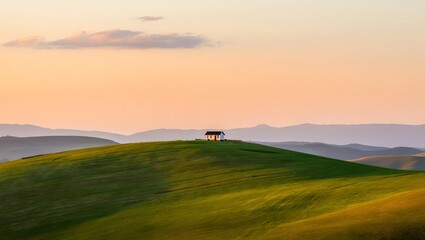 Obraz premium House on a hill at sunset with rolling green hills and a soft pastel sky above