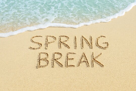 "Spring Break" message written in sand, with gentle ocean waves lapping.