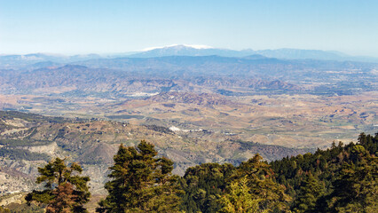 Wide view of a valley with a snow-capped mountain range in the distance. Andalusian landscape.