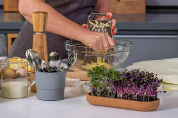 Female chef grating fresh ingredients into a glass bowl, surrounded by kitchen utensils, herbs, and a modern cooking environment, showcasing culinary creativity and preparation with copy space