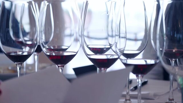 Tasting different types of exclusive aged red wine on special event in restaurant, wineglasses on banquet table for degustation, unrecognisable person making notes on sheep paper rating wine taste