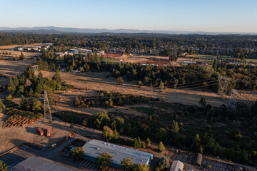 Aerial drone photo of Oregon City landscape at sunset featuring power lines, transmission towers, roads, buildings, forest areas, and open fields under warm autumn evening light