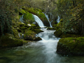 Magical forest creek with waterfall and moss - A beautiful scene of a silky waterfall and creek flowing through a lush forest with moss-covered rocks and a natural frame.
