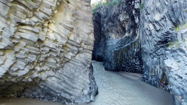 Aerial 4k drone footage of Gole Alcantara gorge in Sicily, Italy, showing the Alcantara river flowing through dramatic basalt rock formations, steep cliffs, and stunning natural landscape shaped by vo