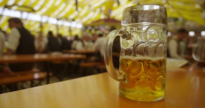 beer mug against blurred background of a beer tent with guests drinking and celebrating at Oktoberfest