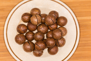 Whole macadamia nuts with sawn shells on saucer, top view