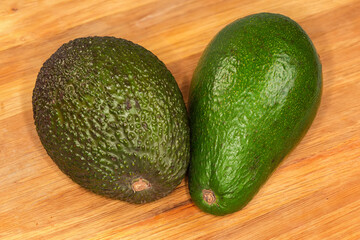 Whole brown Hass avocado and green avocado on wooden surface