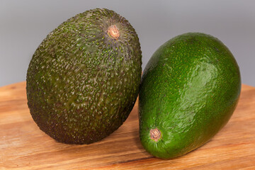 Brown Hass avocado and green ordinary avocado on wooden surface