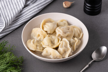 A bowl of dumplings sits on a grey countertop, accompanied by fresh herbs and garlic