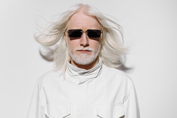 Portrait of a stylish older man with long white hair and sunglasses, wearing a white jacket, against a plain white background, exuding a modern and confident vibe