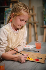 Girl enjoys painting in a workshop. Children drew a picture in art class. Art lesson. Girl mixed and combined colors. Education and learning concept. School kid drawing with brush on easel. Closeup.