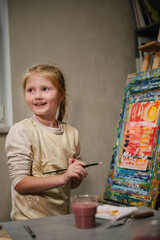 School kid drawing with brush landscapes on easel. Mix and combine colors. Child drew a picture in art class. Girl enjoys painting in a workshop. Art lesson. Education and learning concept.