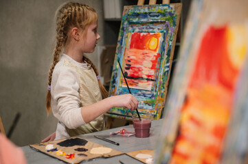 Girl enjoys painting in workshop. Art lesson. Education and learning concept. Child draw a picture in art class. School kid drawing with brush landscapes on easel. Mix and combine colors.