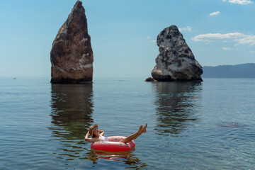 Woman, ocean, relaxing on an inflatable donut ring in calm water by scenic sea stacks, summer leisure.