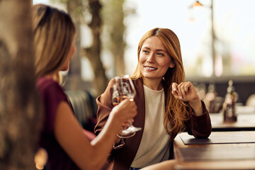 Two Women Socializing in an Outdoor Cafe with Drinks and Smiling Expressions