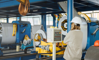 Industrial equipment for working with coil metal. Decoiler holds and unwinds metal coil. Slitting or cut-to-length line - cut coil metal into strips. Woman wearing helmet is working there