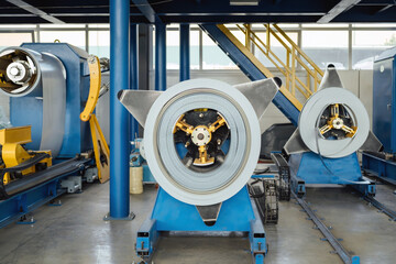 Industrial equipment for working with coil metal. Decoiler holds and unwinds metal coil. Slitting or cut-to-length line - cut coil metal into strips. Crane with hook - used for moving coils.