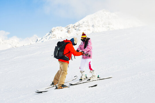 Male Ski instructor in red jacket assisting hold hands beginner female adult skier in pink outfit on snowy mountain slope, concept of ski school, training, winter tourism and lifestyle