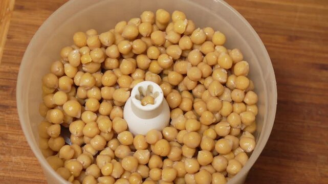 Chickpeas Food Processor Cooking. A hand adds cooked chickpeas to a kitchen appliance for preparing a healthy meal.