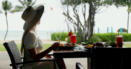Woman dining outdoors at tropical beach resort, enjoying meal with refreshing drinks, summer...