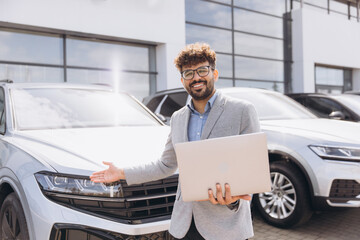 Arab businessman holding laptop presenting new car