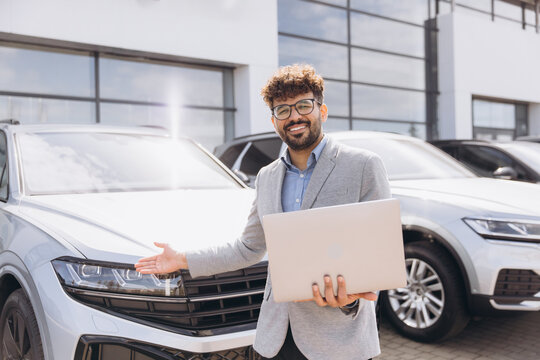 Arab businessman holding laptop presenting new car - Powered by Adobe