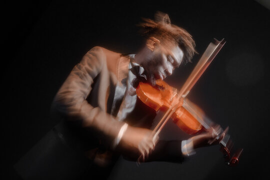 Black young adult man playing violin on stage, wearing formal suit, captured in motion blur, focusing intently on instrument, dramatic lighting highlighting facial features